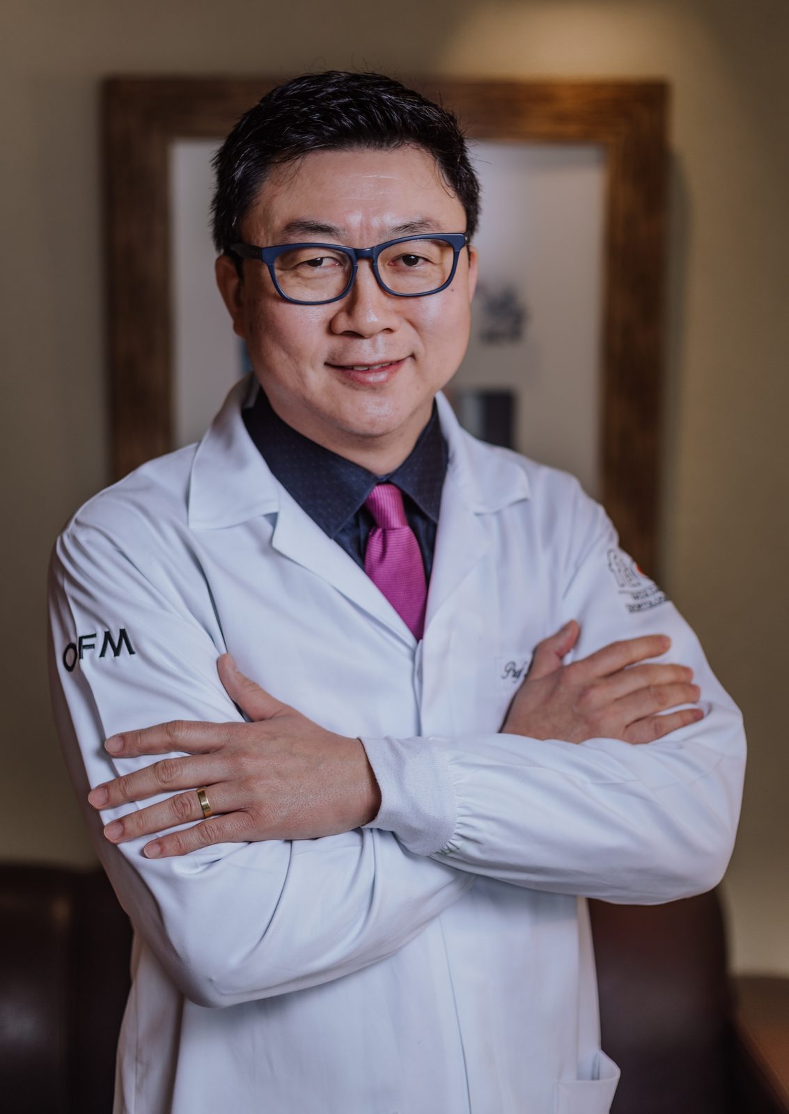 Dr. Wagner Okai, cirurgião-dentista, de jaleco branco e braços cruzados, sorrindo